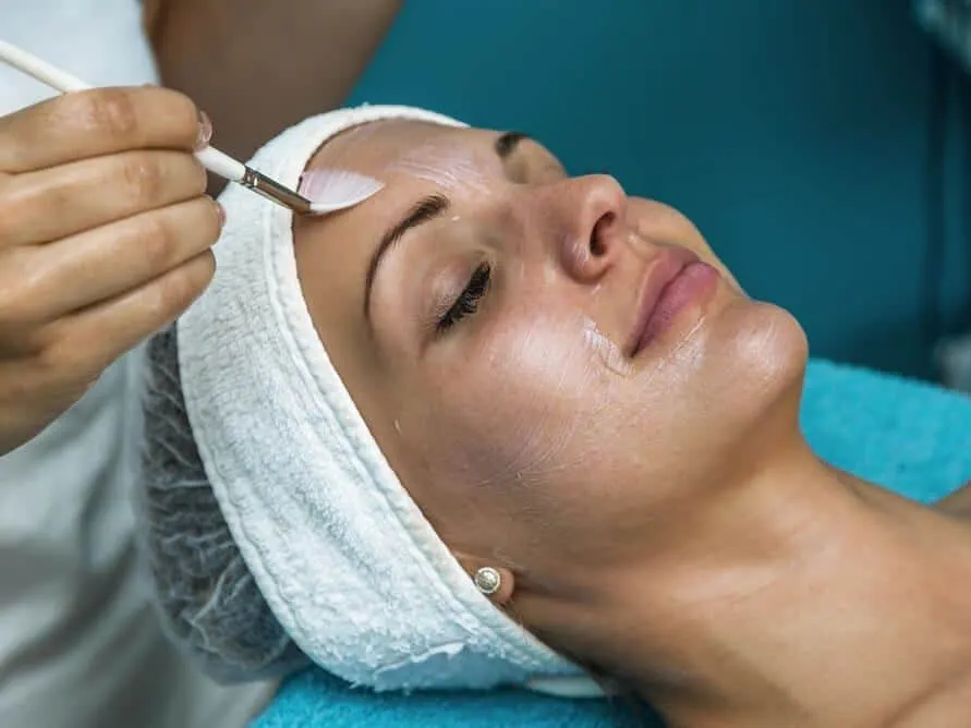 Stock photograph of a model: a woman with a towel around her hair has a peel applied to her forehead with a brush