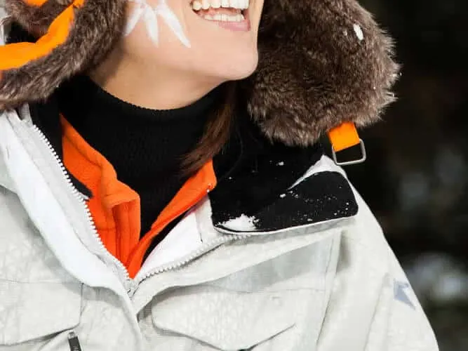 Stock photograph of a model: a smiling woman in a fur-lined hat, ski goggles and a white jacket against a snowy background