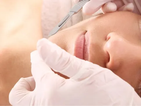 Stock photograph of a model: woman lying back as gloved hands hold a small blade near her face.