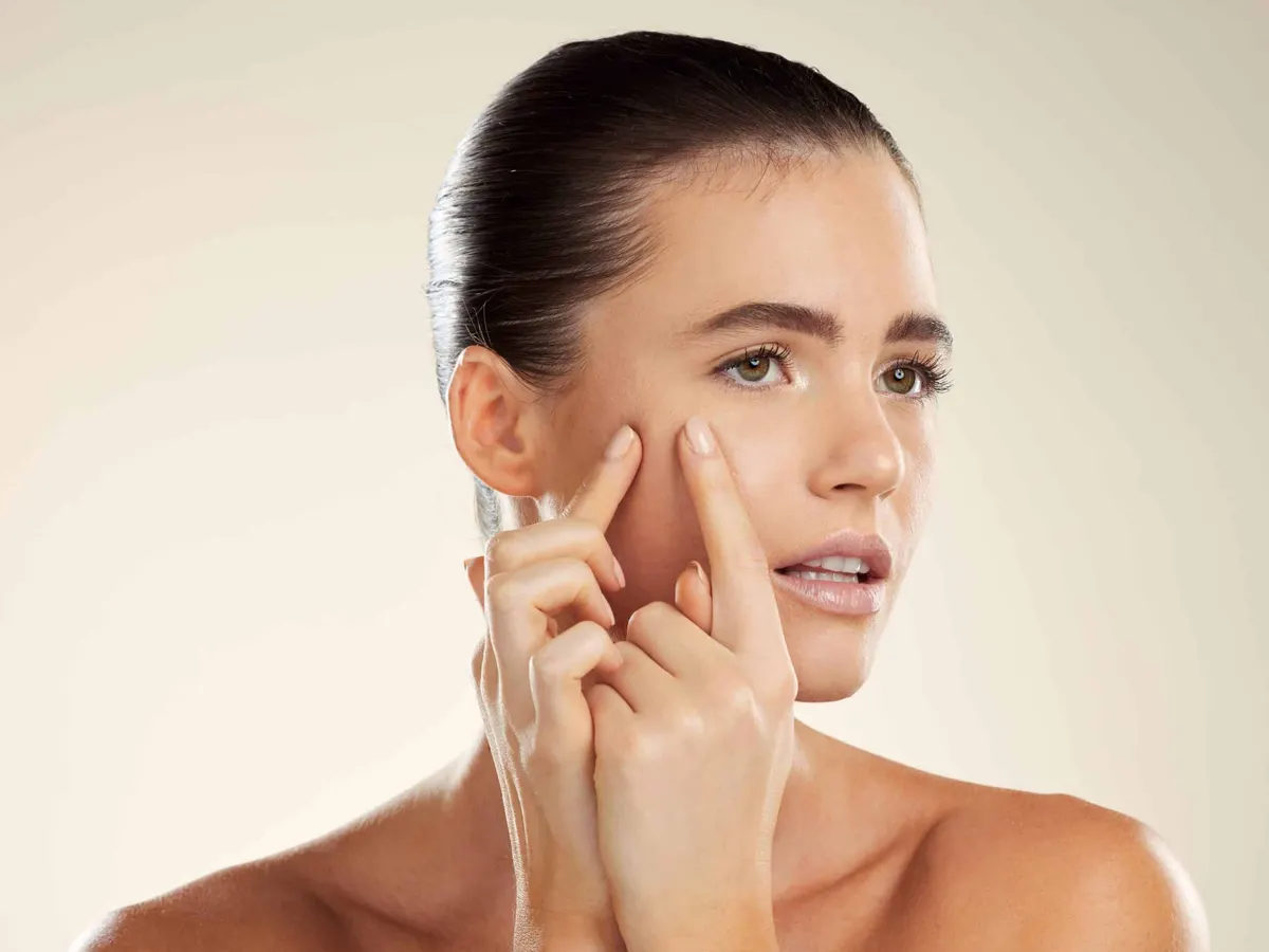 Stock photograph of a model: a woman with her hair pulled back looks aside and presses her fingers to her cheek