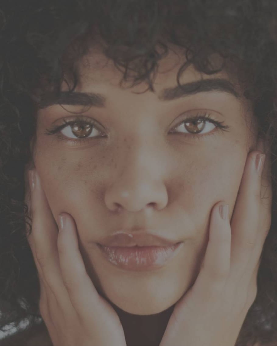Stock photograph of a model: a woman with curly hair and clear skin holds her face in both hands