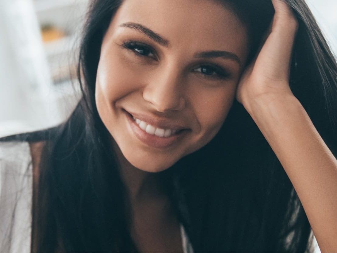 Stock photograph of a model: a smiling woman with long dark hair rests her head on her hand