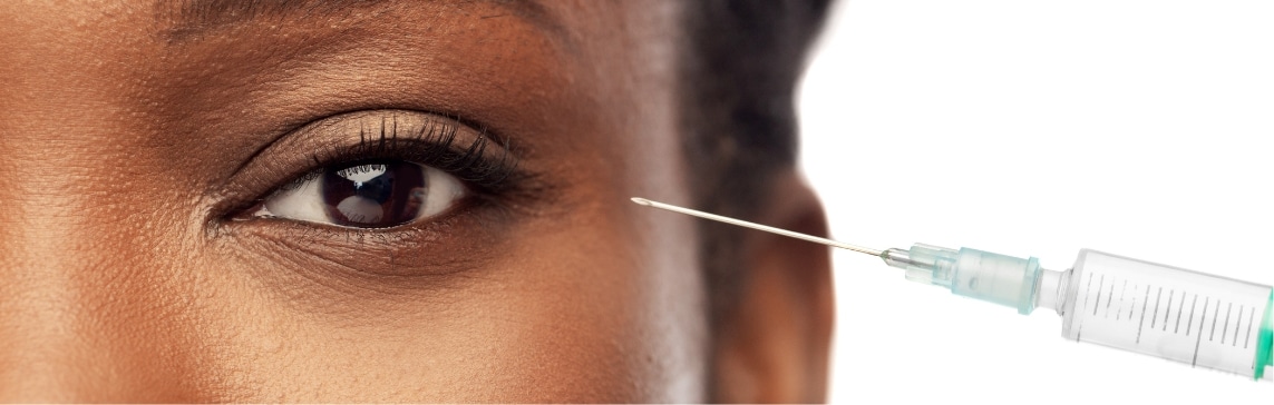 Stock photograph of a model: close-up of a woman's eye with a syringe needle held near her temple.