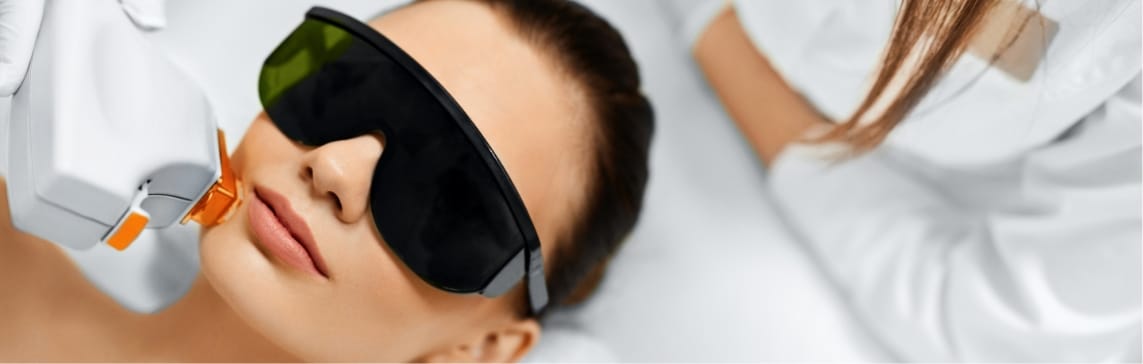 Stock photograph of a model: woman in dark protective eyewear receiving a handheld laser treatment near her chin.