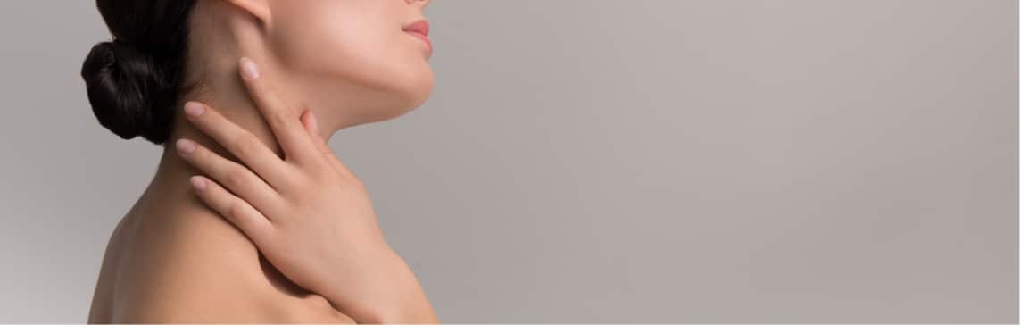Stock photograph of a model: woman in profile against a gray background with one hand resting on her neck.