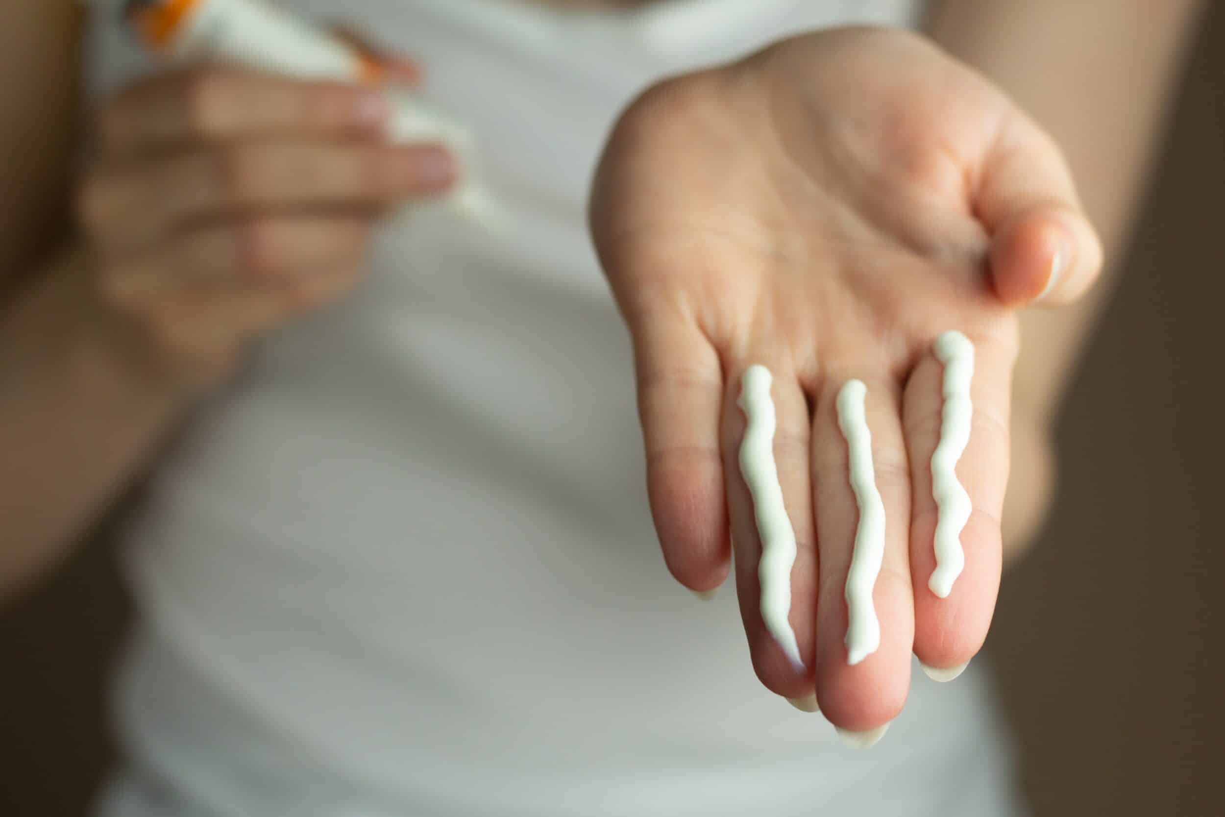 Stock photograph of a model: three lines of white sunscreen squeezed onto the fingers of an open hand